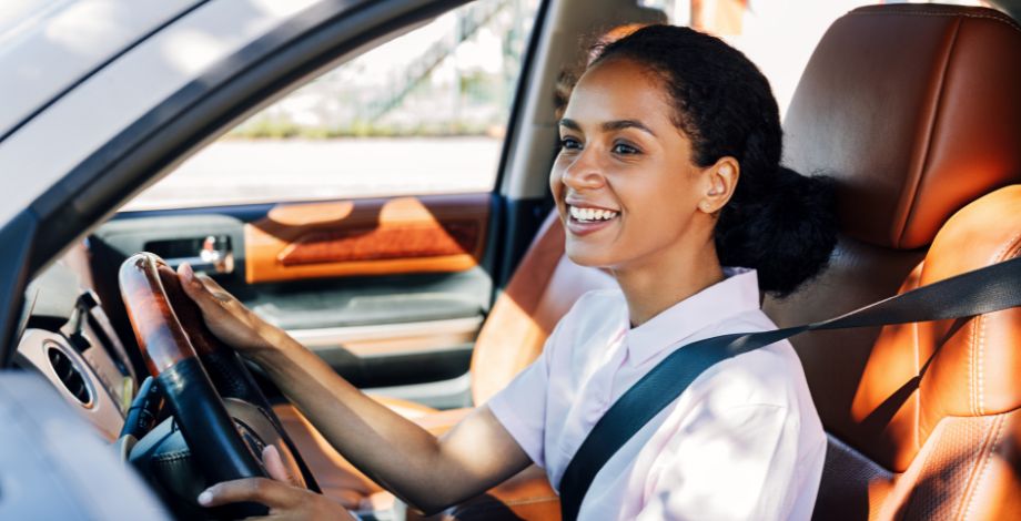 Mujer joven sonriendo, sentada en el asiento del conductor de un vehículo.