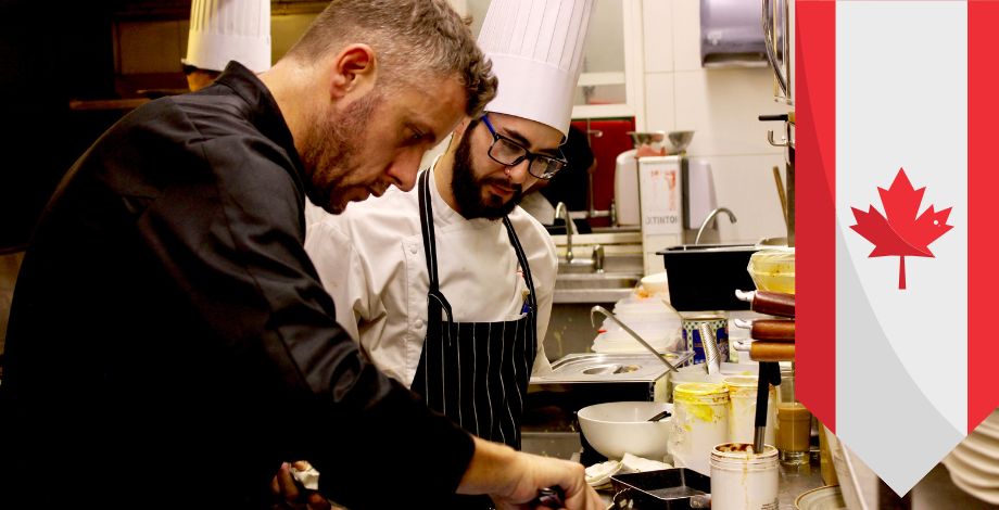 Chef y asistente trabajando juntos. Bandera de Canadá en el costado derecho de la foto.