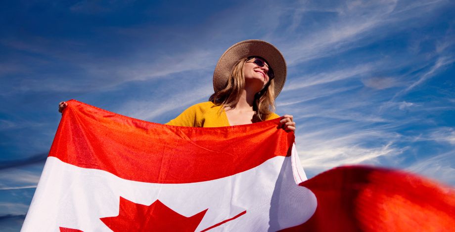 Mujer con bandera canadiense en manos y de fondo un cielo azul