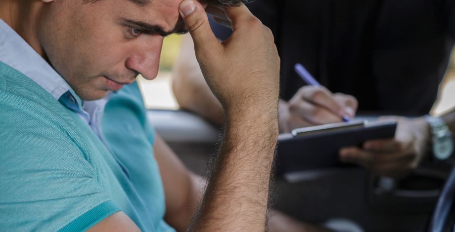 Hombre preocupado en su carro, siendo multado por un oficial.